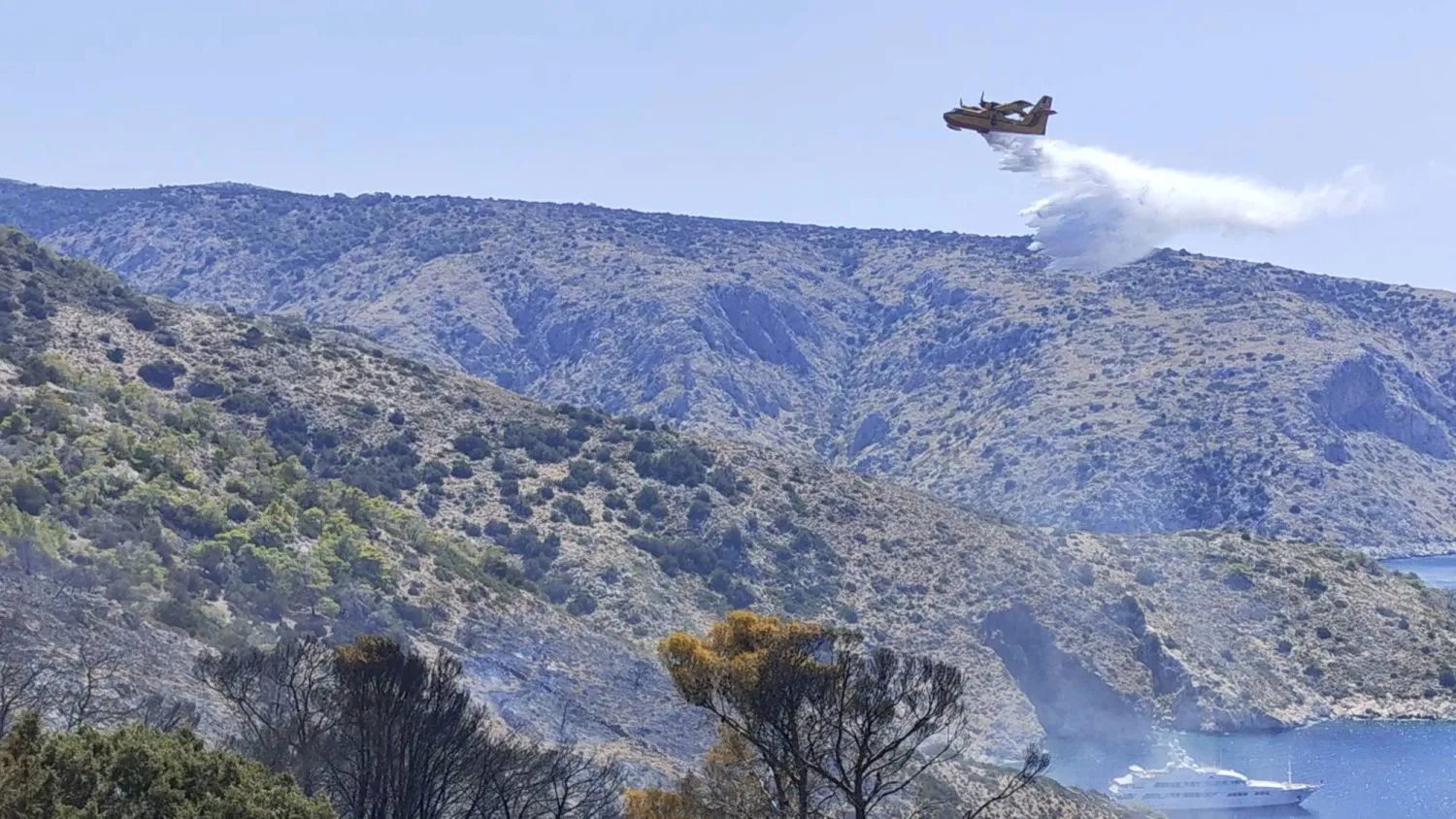 A firefighting plane drops water over an area affected by a forest fire on the island of Hydra, Greece June 22, 2024 in this screen grab from social media video. Volunteer fire station of Hydra/Handout via REUTERS 