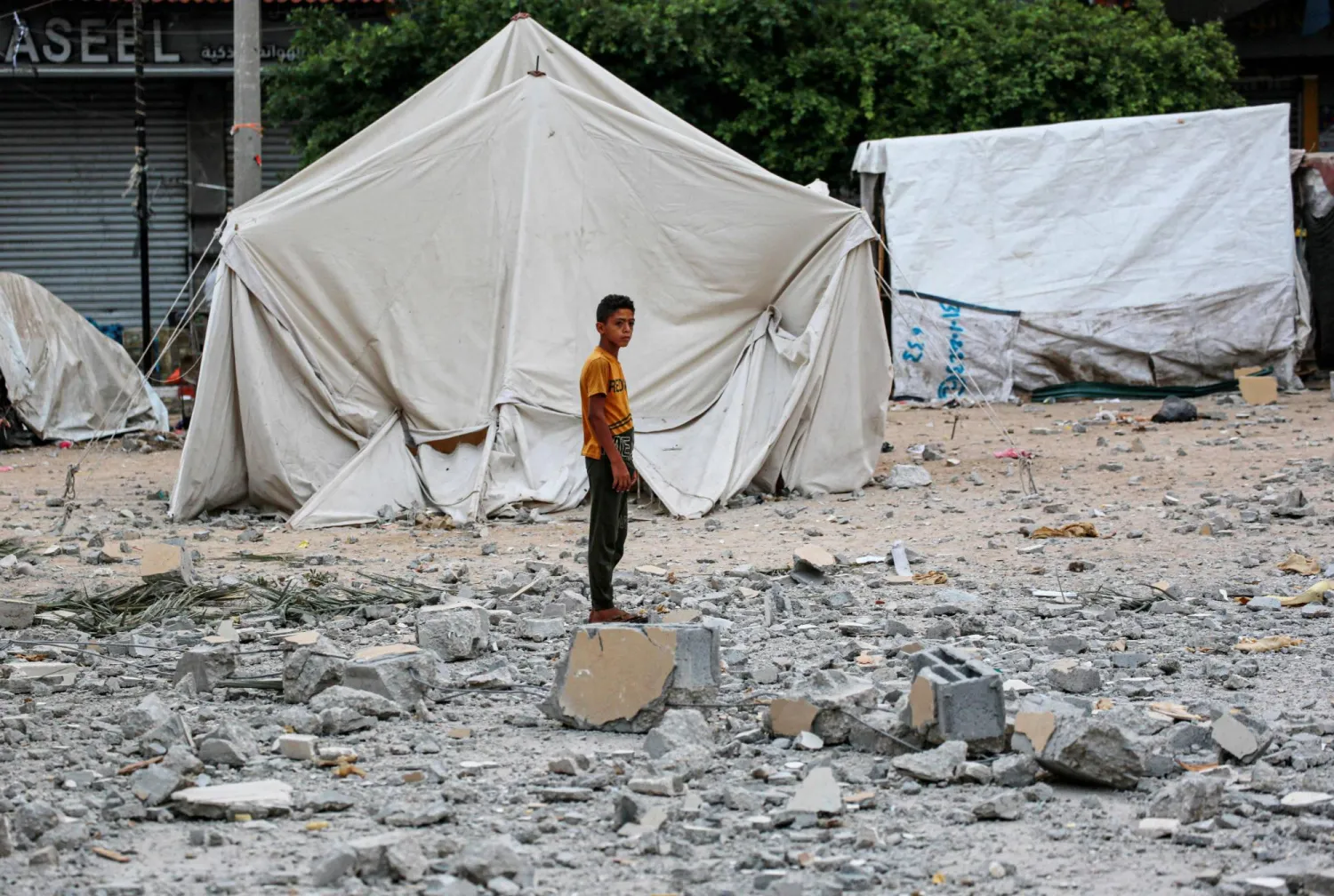 A Palestinian youth stands on rubble close to tents housing internally displaced people, erected in the square near the Deir al-Balah municipality building, destroyed following Israeli bombardment of Deir al-Balah, in the central Gaza Strip on June 28, 2024. (Photo by Bashar TALEB / AFP)