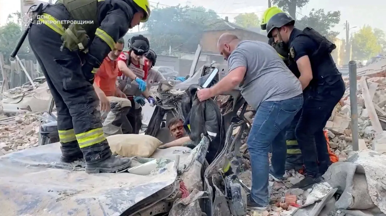 عناصر من الدفاع المدني تحاول إنقاذ رجل مصاب داخل سيرة مدمرة قرب مبنى سكني استهدفته غارة روسية في دنيبرو بأوكرانيا (رويترز)