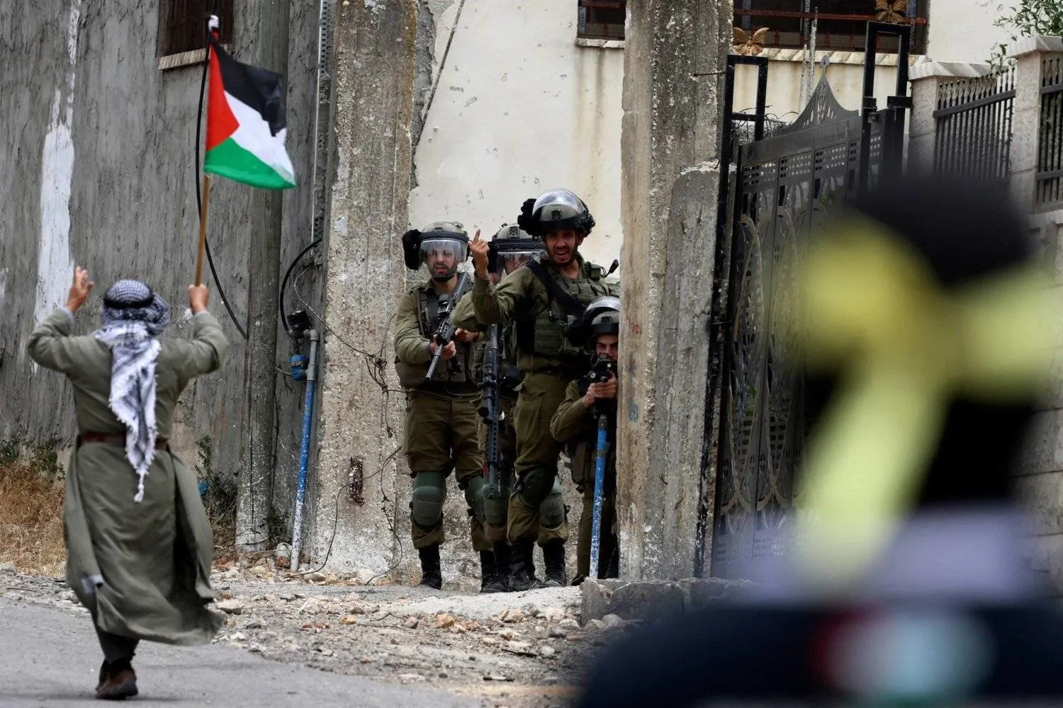 A demonstrator brandishing a Palestinian national flag walks past Israeli troops, during confrontations with them following a protest against the expropriation of Palestinian land by Israel in the occupied-West Bank, in the village of Kfar Qaddum, near the Jewish settlement of Kedumim, on June 9, 2023. (Photo by Jaafar ASHTIYEH / AFP)