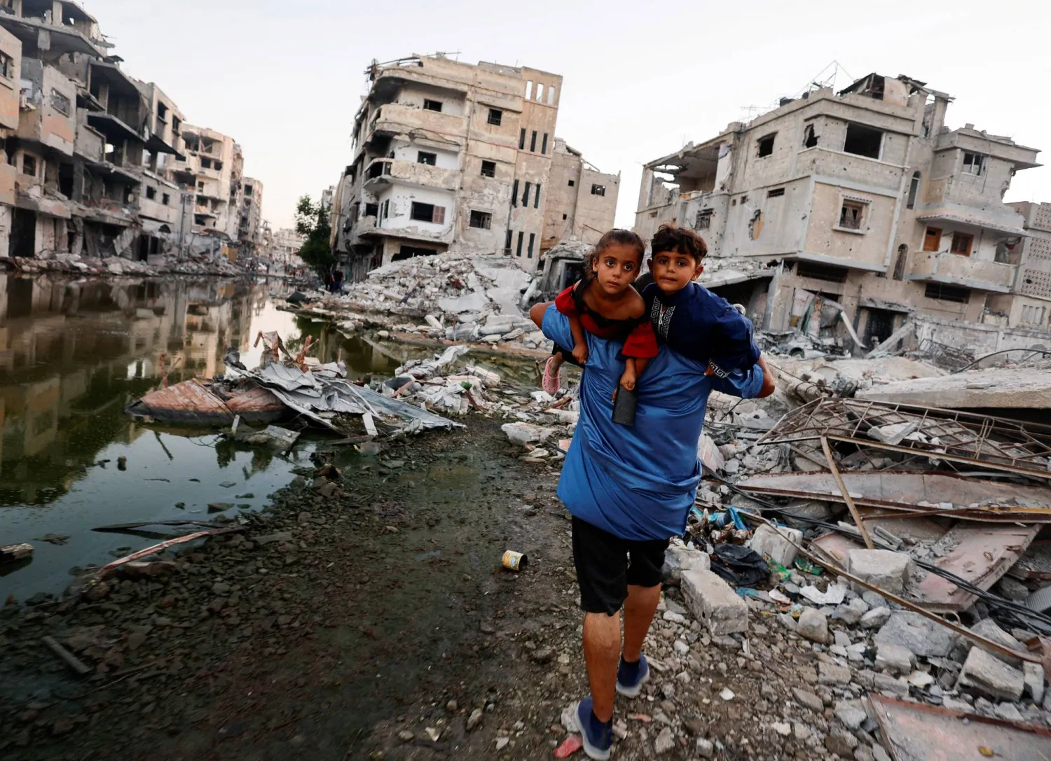 A Palestinian man holds his children as he walks next to buildings destroyed in an Israeli strike, amid the ongoing conflict between Israel and Hamas, in Khan Younis, in the southern Gaza Strip, June 30, 2024. REUTERS/Mohammed Salem   