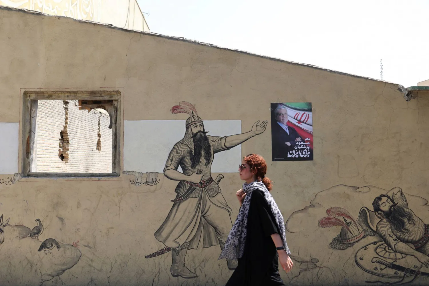 إيرانية دون حجاب تمر أمام ملصق بزشكيان وُضع فوق جدارية في شارع وسط طهران (رويترز)