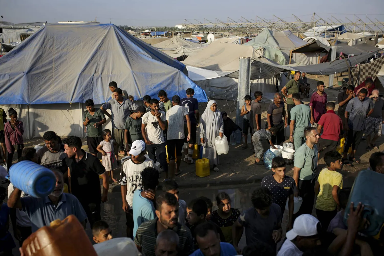 Palestinians displaced by the Israeli bombardment of the Gaza Strip queue for water at a makeshift tent camp in the southern town of Khan Younis, Monday, July 1, 2024. (AP Photo/Jehad Alshrafi)