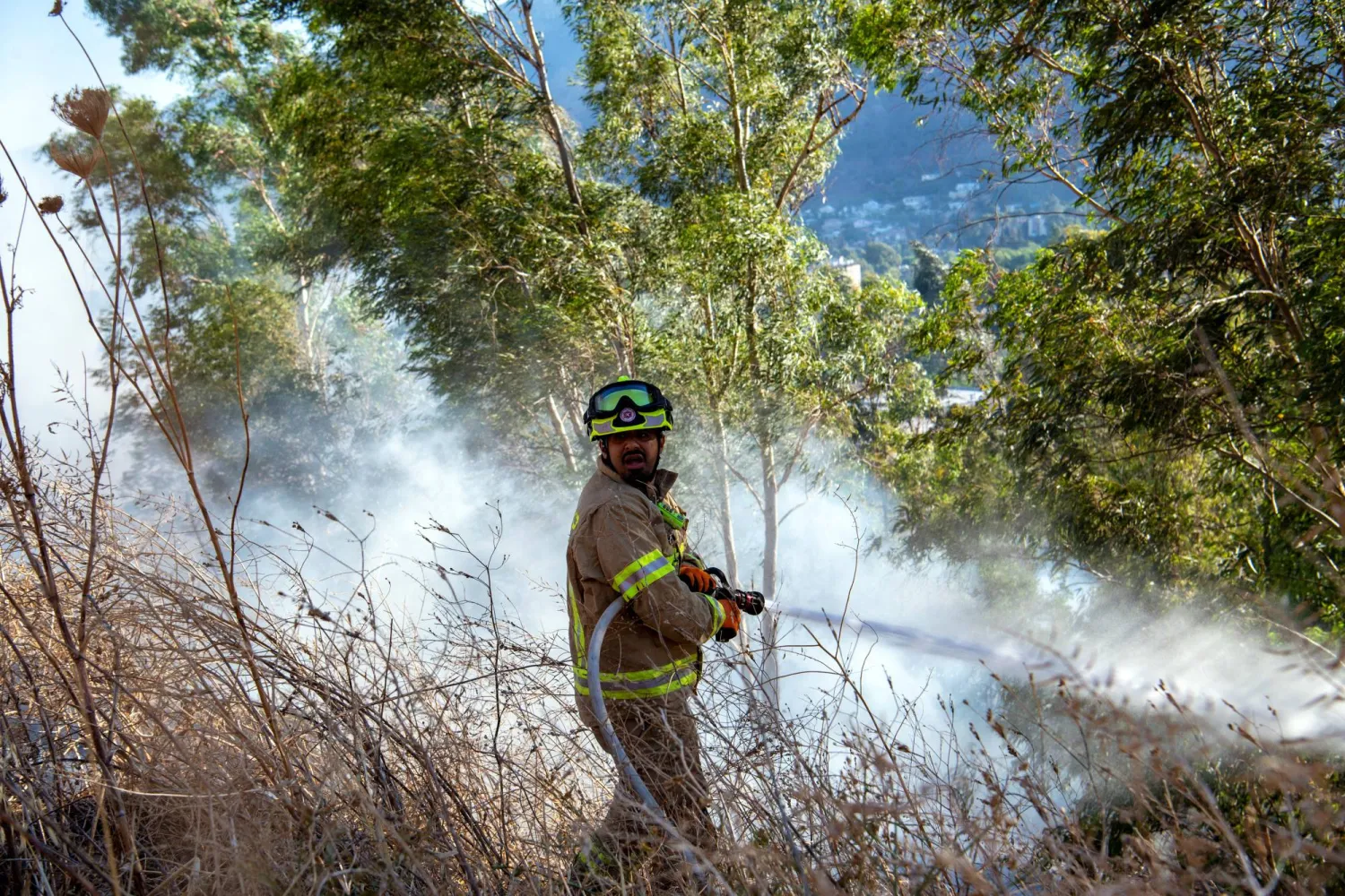 رجل إطفاء إسرائيلي يعمل على إطفاء الحرائق الناتجة عن الصواريخ الحدودية المنطلقة من لبنان خارج كريات شمونة في شمال إسرائيل (رويترز)