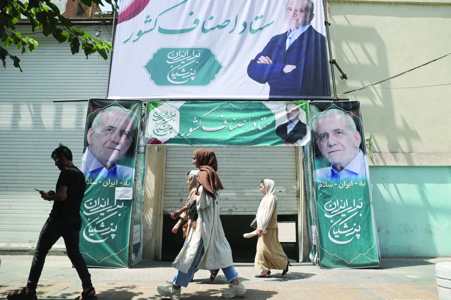 İranlılar aday Mesud Pezeşkiyan'ın afişlerinin önünden geçiyor (Reuters)