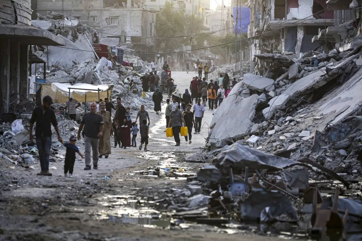 Palestinians displaced by the Israeli air and ground offensive on the Gaza Strip, walk through a dark streak of sewage flowing into the streets of the southern town of Khan Younis, Gaza Strip, Thursday, July 4, 2024. (AP) 