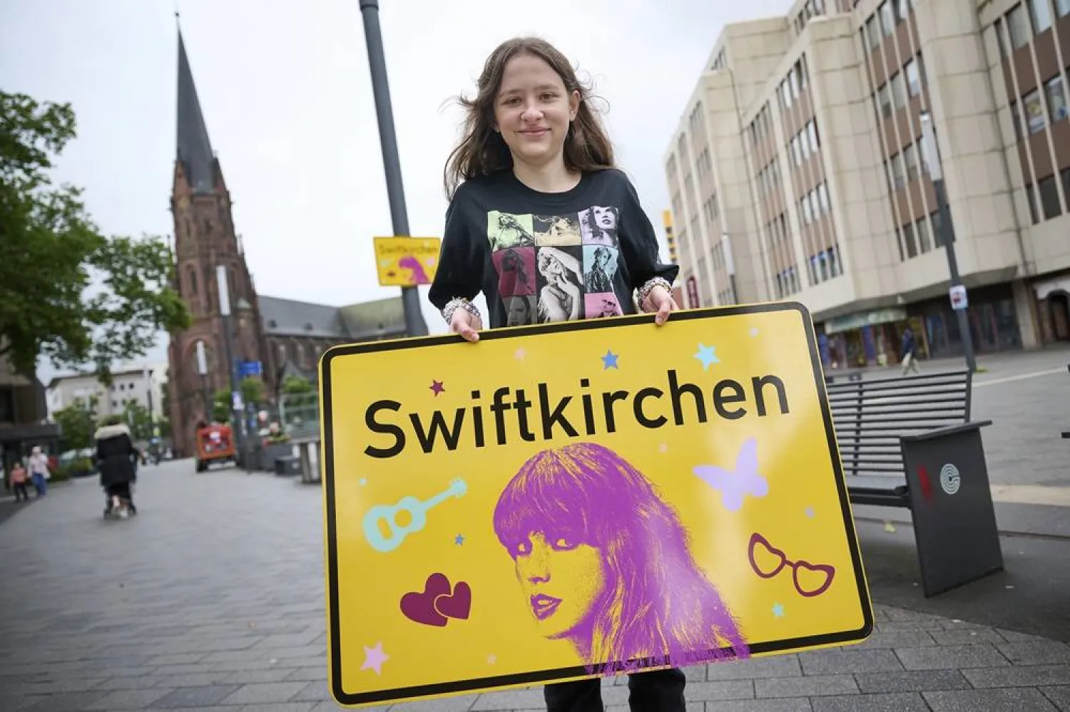 Schoolgirl Aleshanee Westhoff shows a "Swiftkirchen" town sign in honor of musician Taylor Swift in Gelsenkirchen, Germany, Tuesday, July 2, 2024. (dpa via AP)