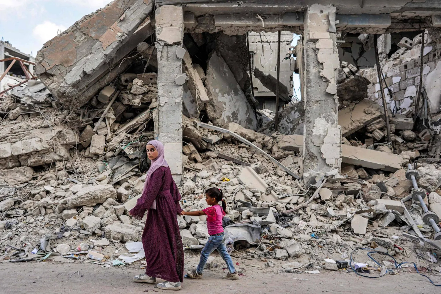 A woman walks with a girl past the rubble of a destroyed building in Khan Yunis in the southern Gaza Strip on July 8, 2024. (Photo by Bashar TALEB / AFP)