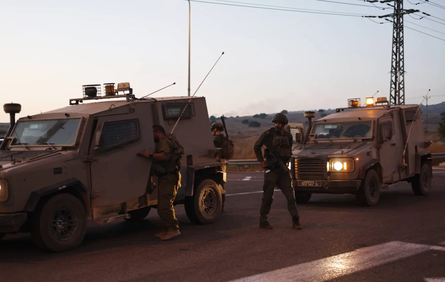 شرطة وجنود إسرائيليون يغلقون طريقاً بينما يتصاعد الدخان في الخلفية بعد إصابة شخصين في سقوط صاروخ بمرتفعات الجولان (إ.ب.أ)