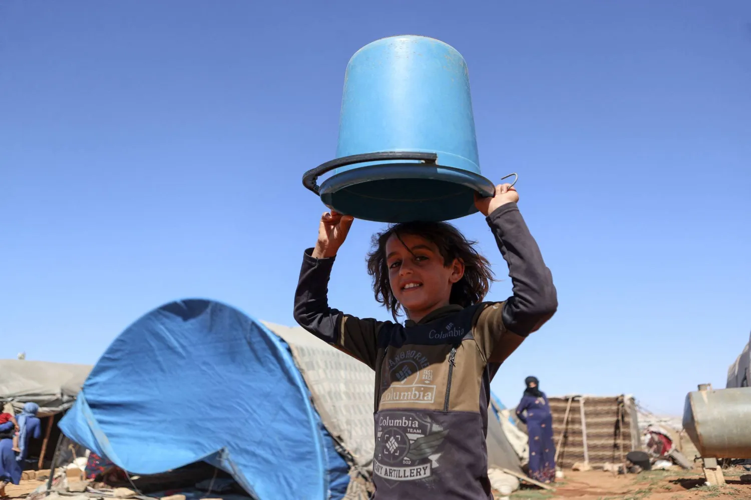 طفل سوري يحمل دلواً فارغاً في مخيم للنازحين بالقرب من سرمدا في محافظة إدلب شمال سوريا (أ.ف.ب)