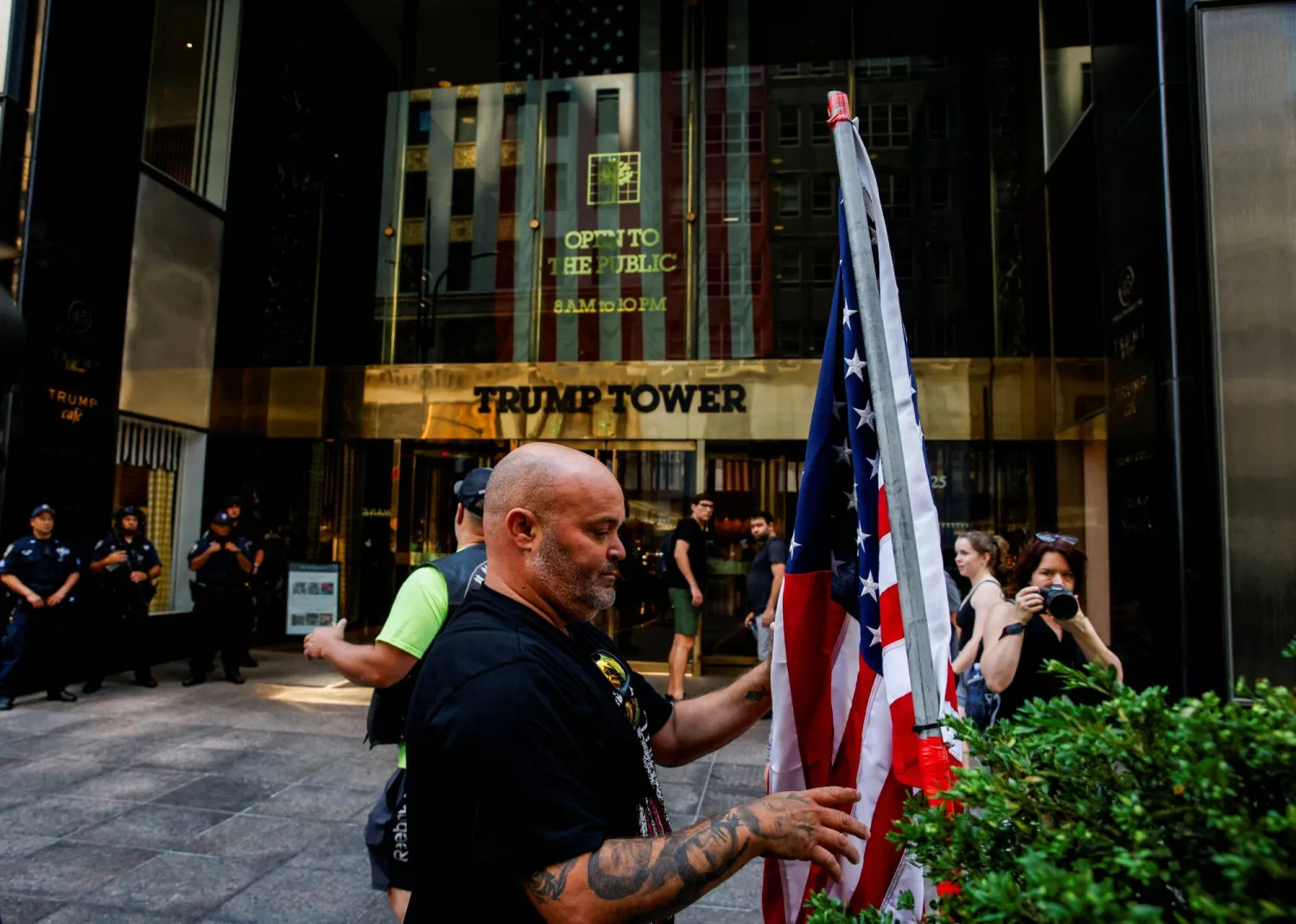 رجل يحمل علم الولايات المتحدة أمام برج ترمب في نيويورك الأحد غداة محاولة اغتيال الرئيس الأميركي السابق (رويترز)
