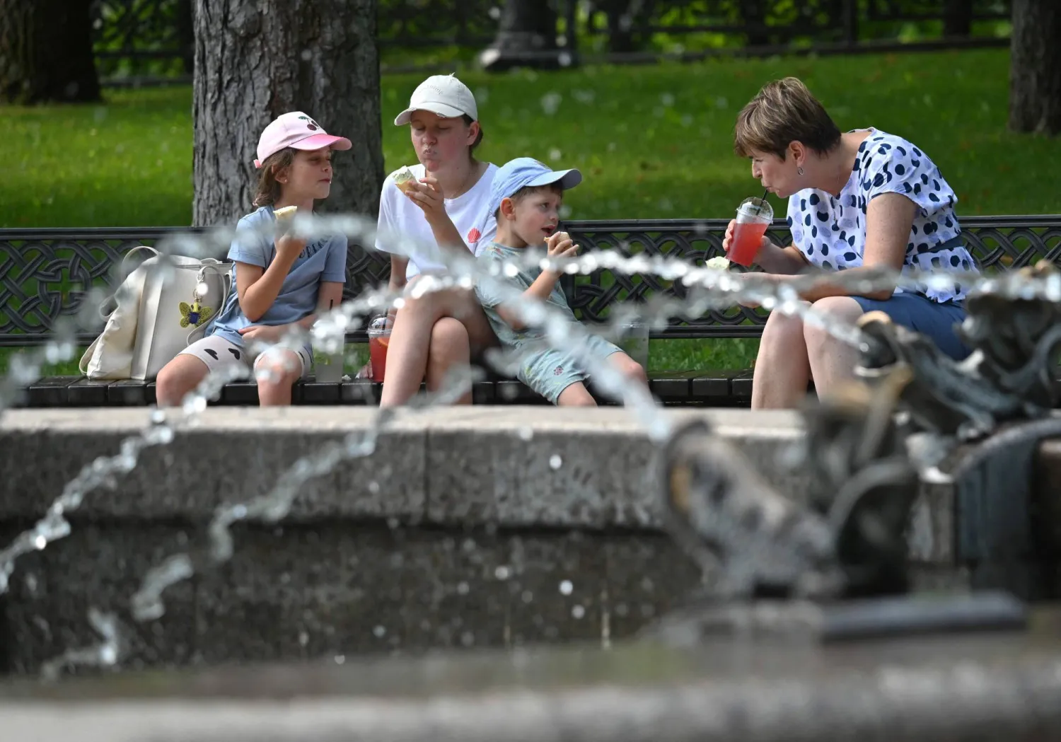 عائلة تتناول الآيس كريم بالقرب من نافورة في حديقة خلال موجة حارة بكييف (أ.ف.ب)