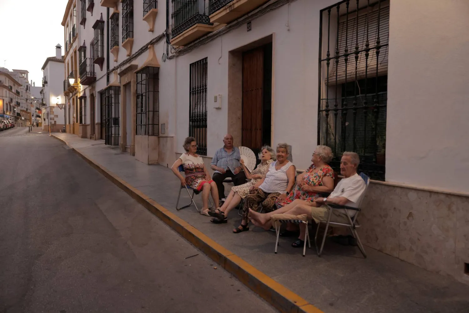 جيران يجلسون أمام منازلهم لتبادل أطراف الحديث والتغلب على الحرارة بإحدى ليالي الصيف الحارة في روندا بإسبانيا  (رويترز)