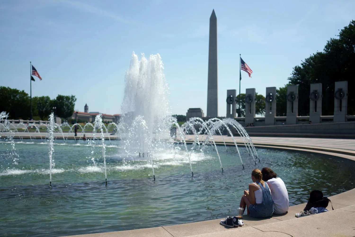أشخاص يجلسون أمام نافورة النصب التذكاري للحرب العالمية الثانية في واشنطن العاصمة (إ.ب.أ)