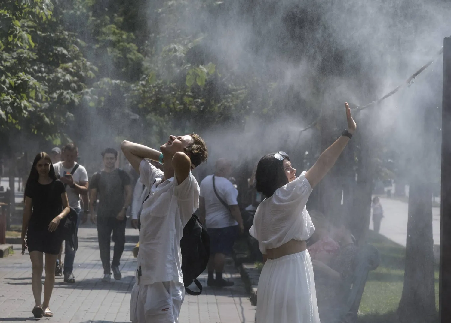 أوكرانيون يبردون أنفسهم بالمياه المرشوشة من الأنابيب المعلقة فوق رصيف بالشارع المركزي في خريشاتيك (إ.ب.أ)