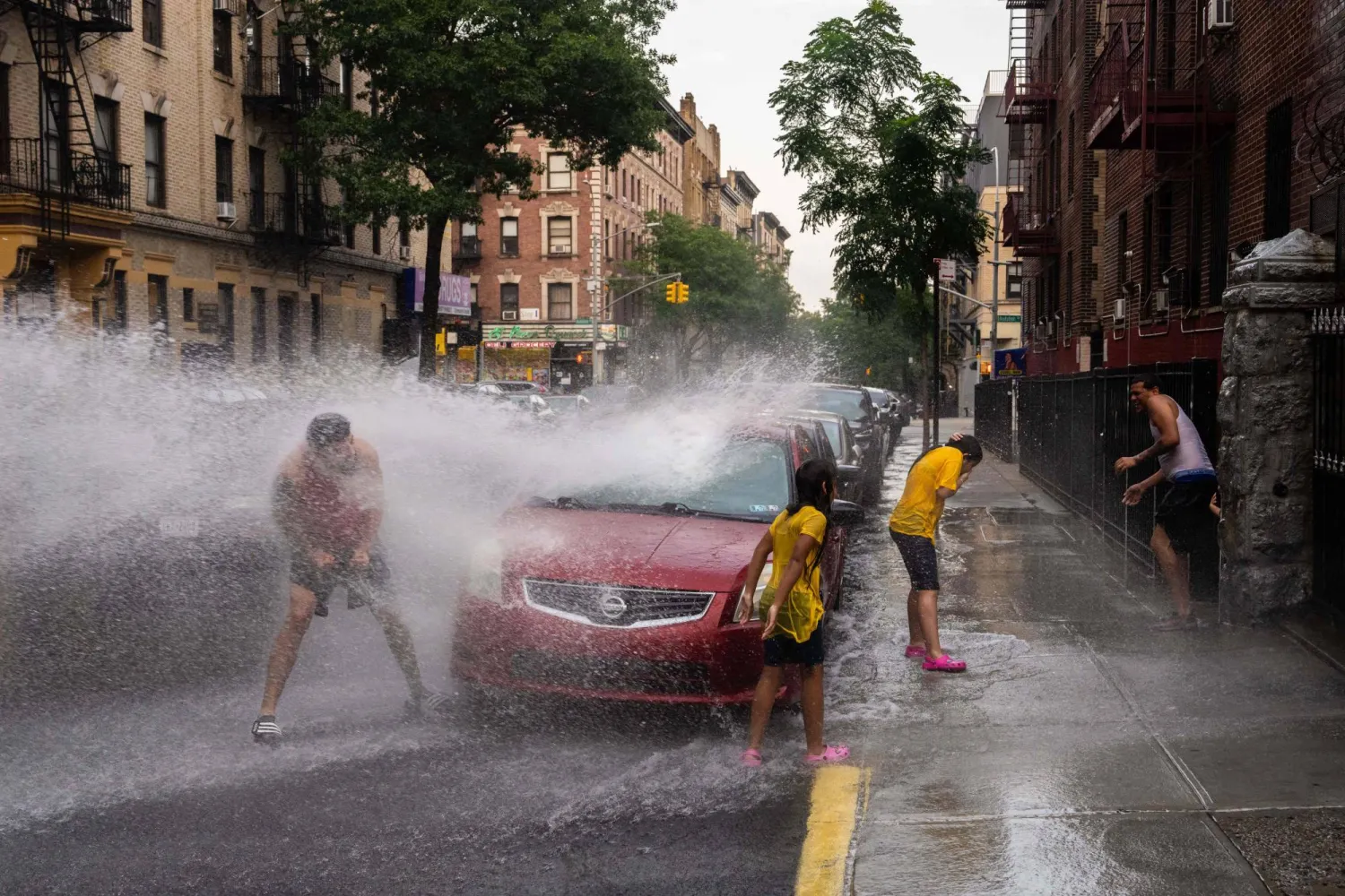 سكان محليون يلعبون بالماء الذي يتم رشه من صنبور إطفاء الحرائق أثناء الطقس الحار في نيويورك (أ.ف.ب)