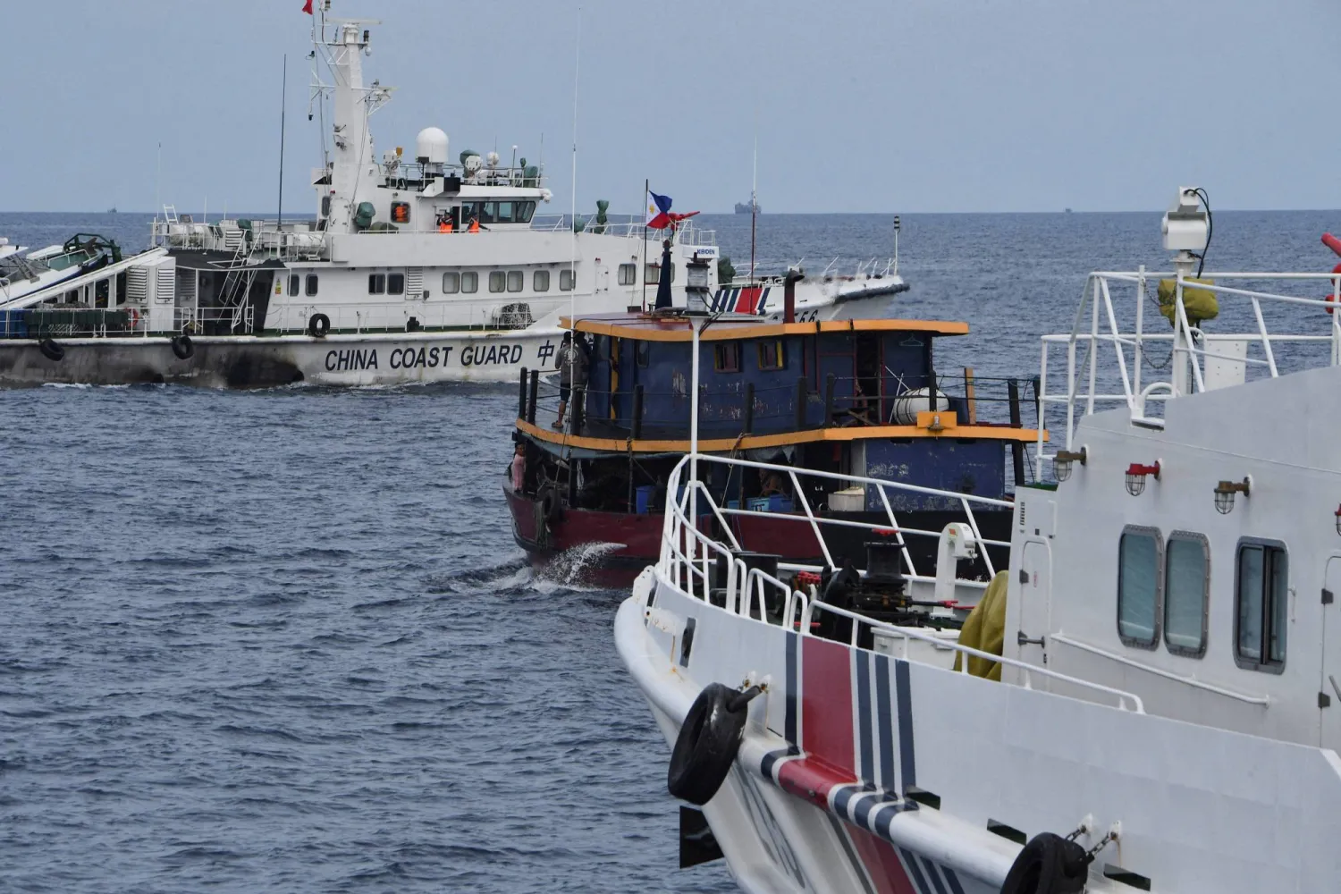 (FILES) This file photo taken on August 22, 2023 shows Chinese coast guard ships (L and R) corralling a Philippine civilian boat chartered by the Philippine navy to deliver supplies to the Philippine navy ship BRP Sierra Madre, in disputed waters of the South China Sea. (Photo by Ted ALJIBE / AFP)