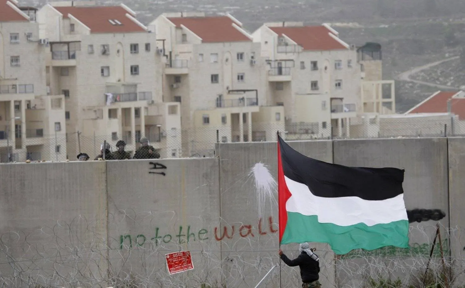 A West Bank Jewish settlement is seen in the background, while a protestor waves a Palestinian flag during a protest against Israel's separation barrier in the West Bank village of Bilin in 2012. (AP)
