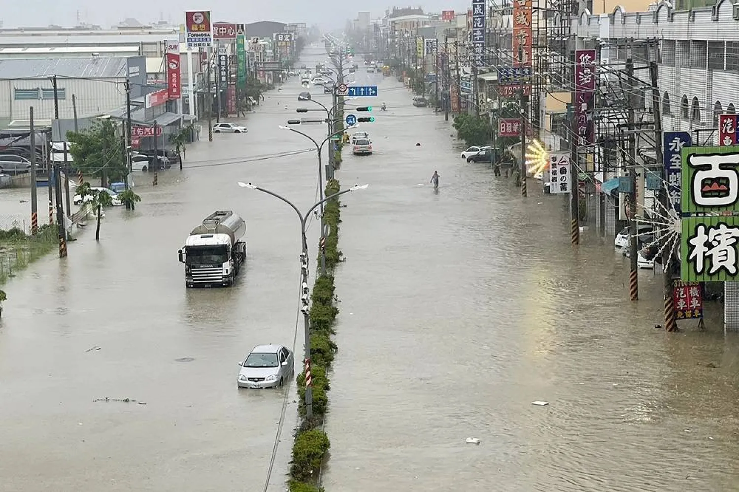 People and vehicles wade through the water along a street that was flooded by Typhoon Gaemi in Kaohsiung on July 25, 2024. (AFP)