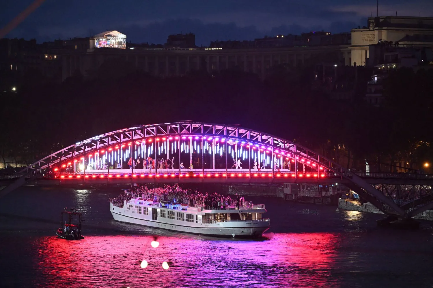 عارضون أعلى قارب يحمل أعضاء وفد فرنسا على طول نهر السين خلال حفل افتتاح دورة الألعاب الأولمبية في باريس 2024 (أ.ف.ب)