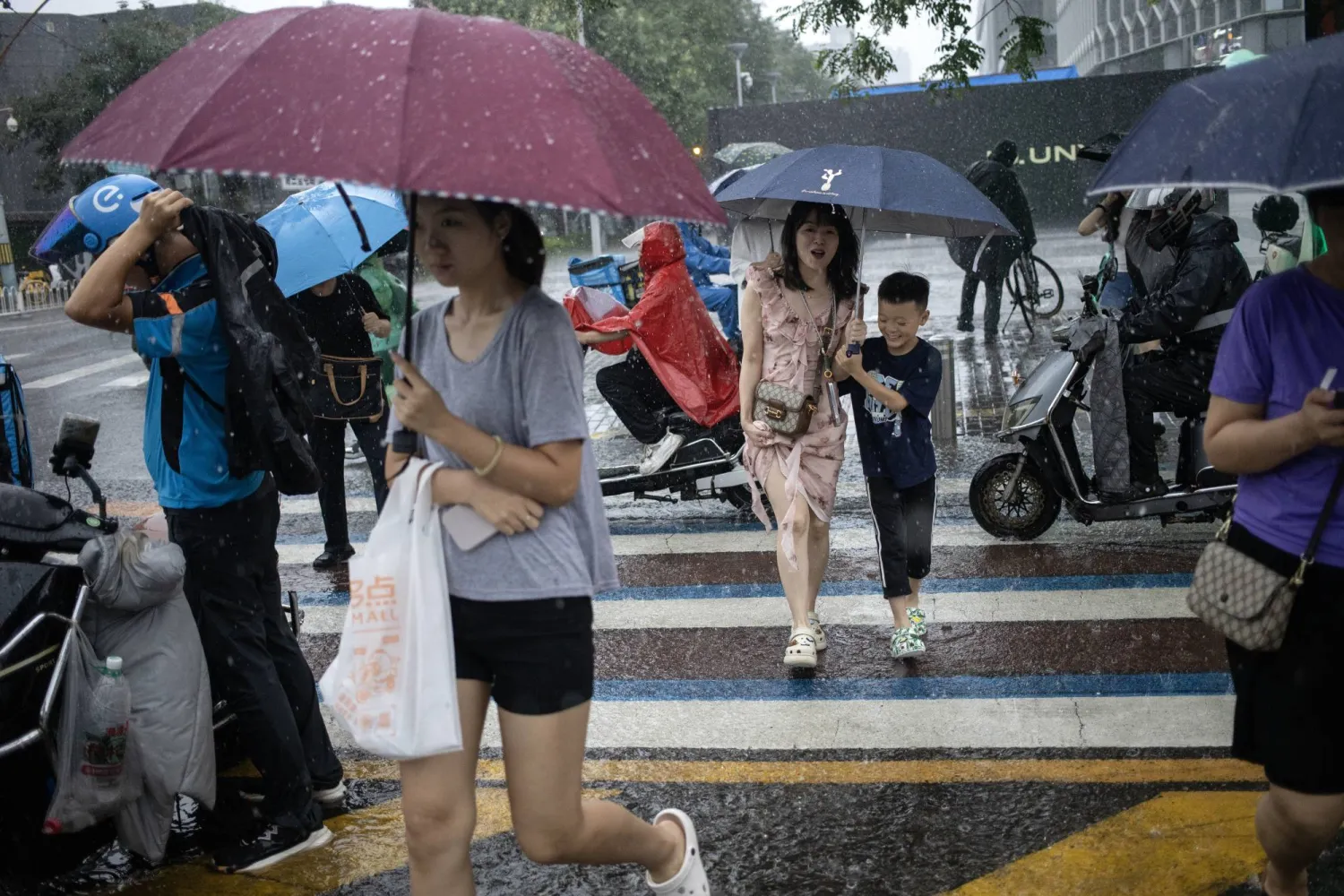 صينيون يستخدمون مظلات خلال هطول أمطار غزيرة في العاصمة بكين (إ.ب.أ)