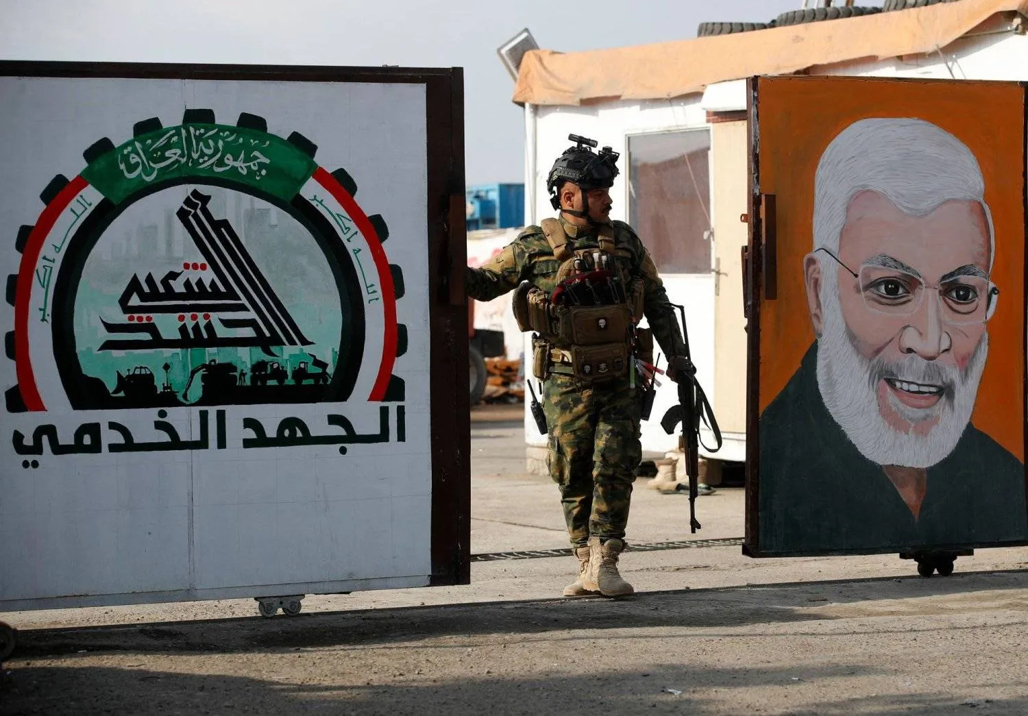 A member of the PMF guards a gate with a mural of slain PMF deputy leader Abu Mahdi al-Muhandis in Baghdad. (AFP) 