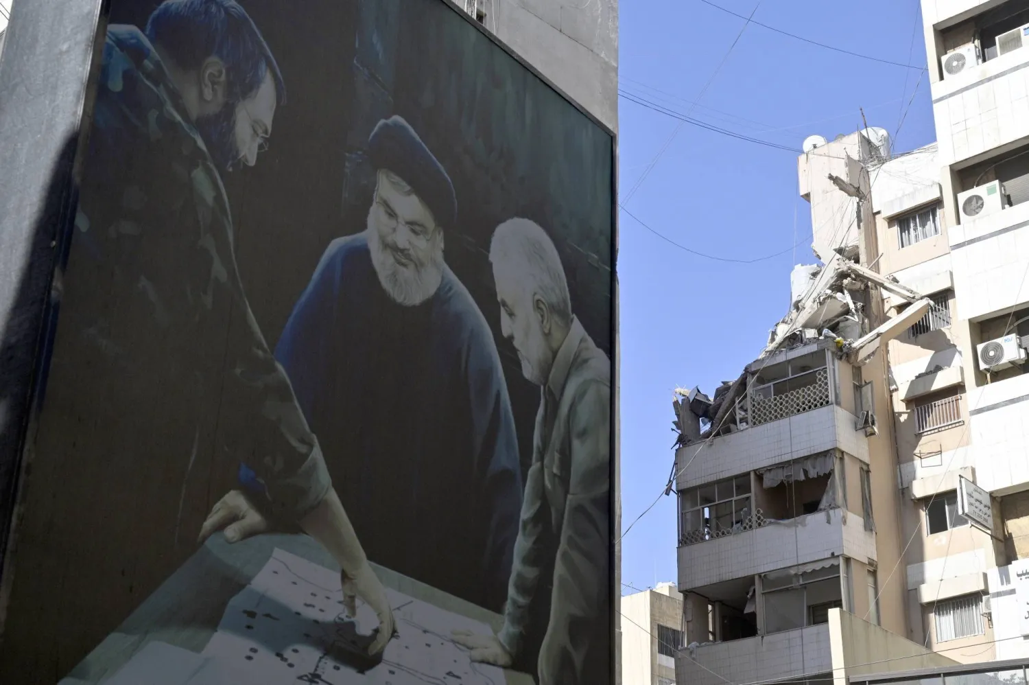 صورة تجمع قاسم سليماني ونصرالله وعماد مغنية مرفوعة على مبنى في ضاحية بيروت الجنوبية قرب موقع الاستهداف الإسرائيلي في حارة حريك (إ.ب.أ)