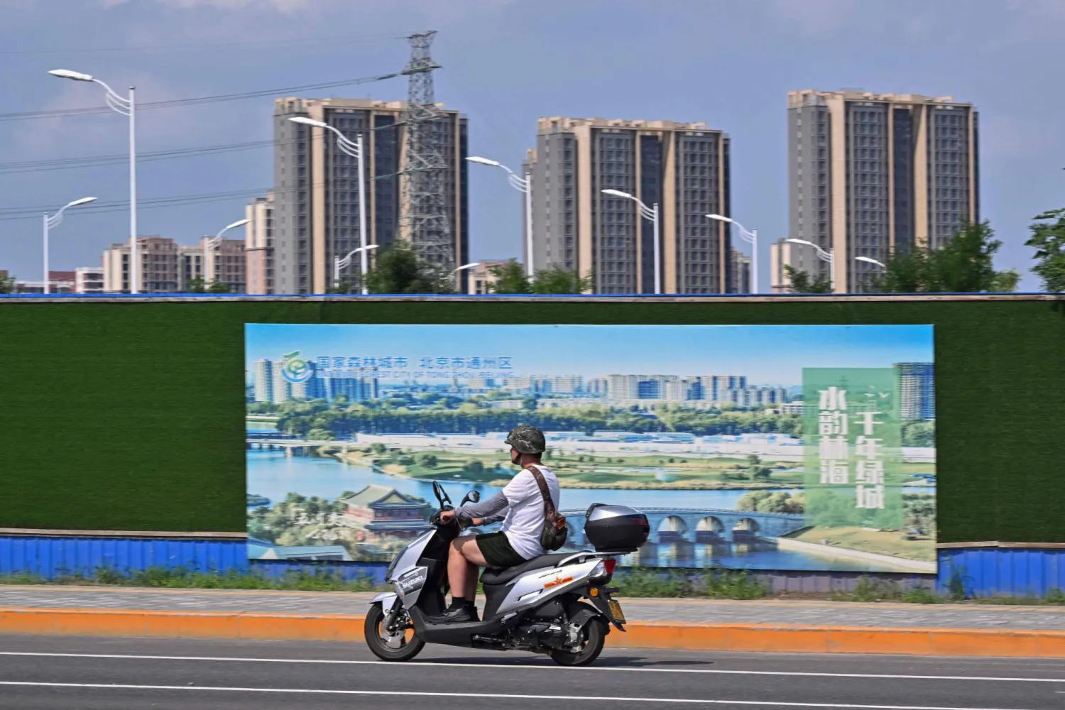 راكب دراجة نارية يمر أمام منطقة أبراج سكنية في العاصمة الصينية بكين (أ.ف.ب)