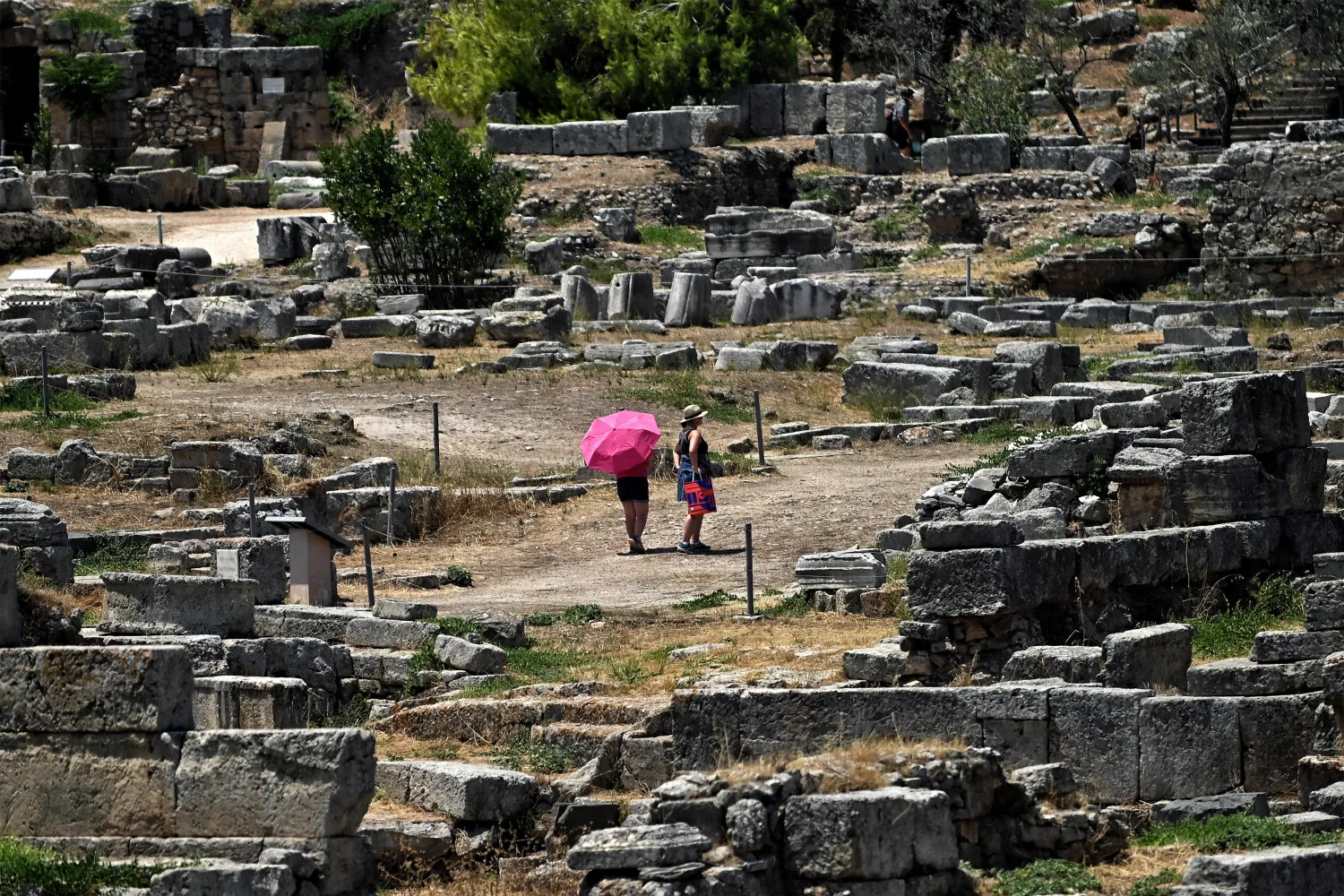 Tourists visit the archaeological site of Ancient Corinthe holding umbrellas, to protect themselves from the strong sun, Greece, 14 July 2024. EPA/VASSILIS PSOMAS