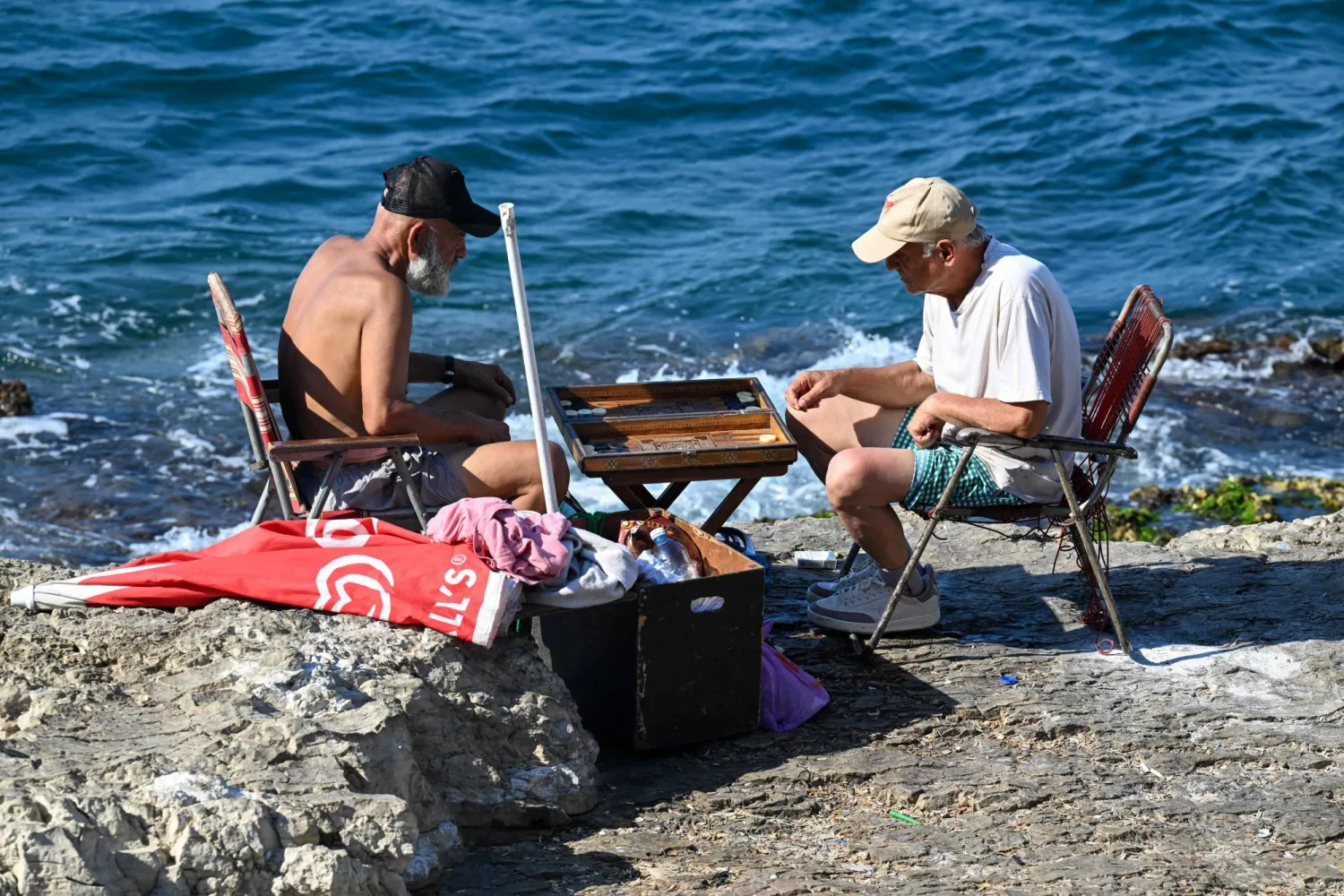 People play backgamon on a rock in Beirut's Ain al-Mreisseh seaside promenade on August 2, 2024. (Photo by JOSEPH EID / AFP)