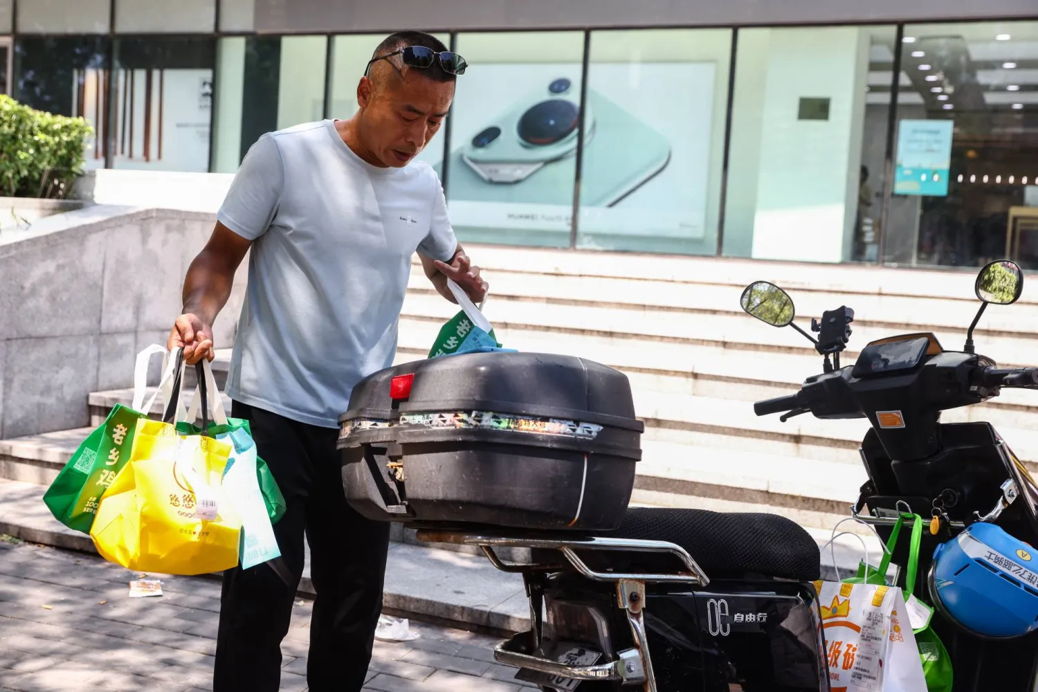 عامل توصيل يحمل طلبات بجوار دراجة نارية في العاصمة الصينية بكين (إ.ب.أ)