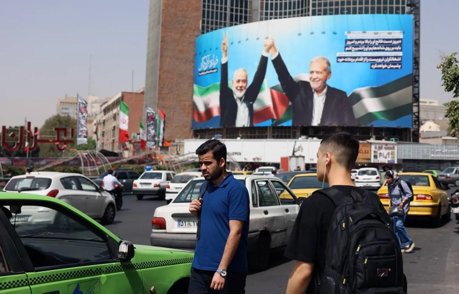 Iranians walk in a road near a billboard depicting Iranian President Masoud Pezeshkian (R) and late Hamas leader Ismail Haniyeh, at Valiasr Square in Tehran, Iran, 05 August 2024. (EPA) 