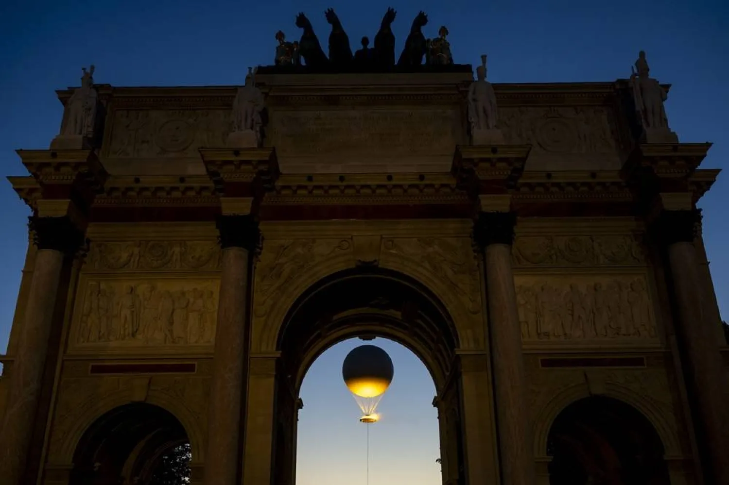 05 August 2024, France, Paris: The Arc de Triomphe du Carrousel with the Paris 2024 Olympic Games' Cauldron, an air balloon, in the background. (dpa)