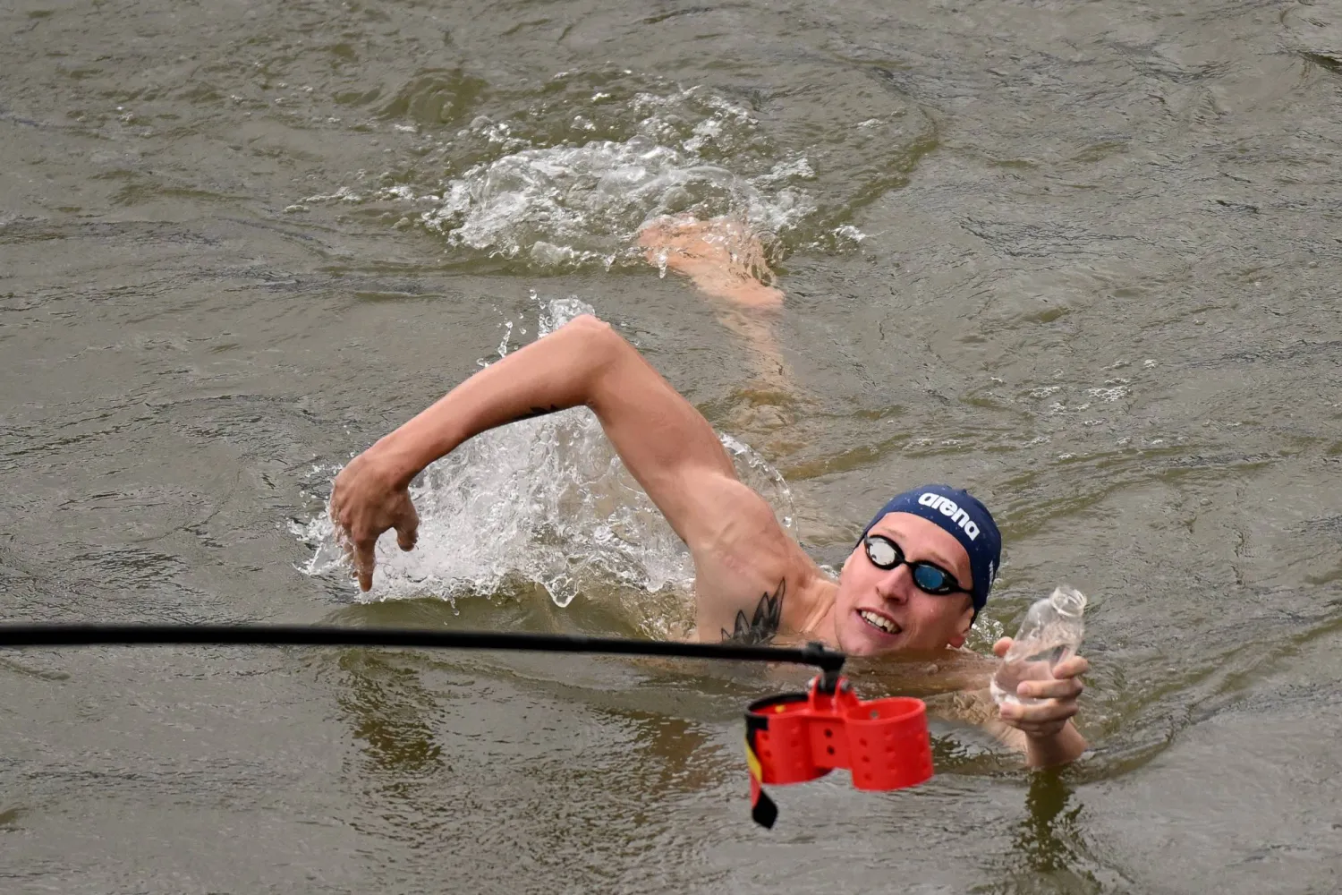 07 August 2024, France, Paris: Germany's Florian Wellbrock fills a bottle with water during the first training session for Olympic open water swimmers in the Seine after it was cancelled over water quality concerns. Photo: Marijan Murat/dpa