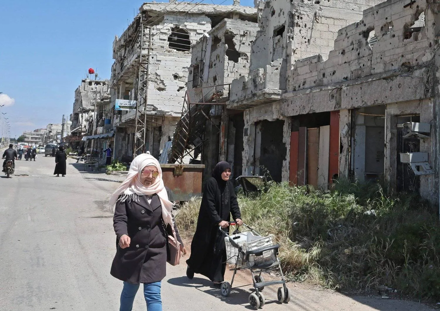 Syrians walk past buildings heavily damaged during Syria's war, in the central city of Homs, April 28, 2020. (AFP)
