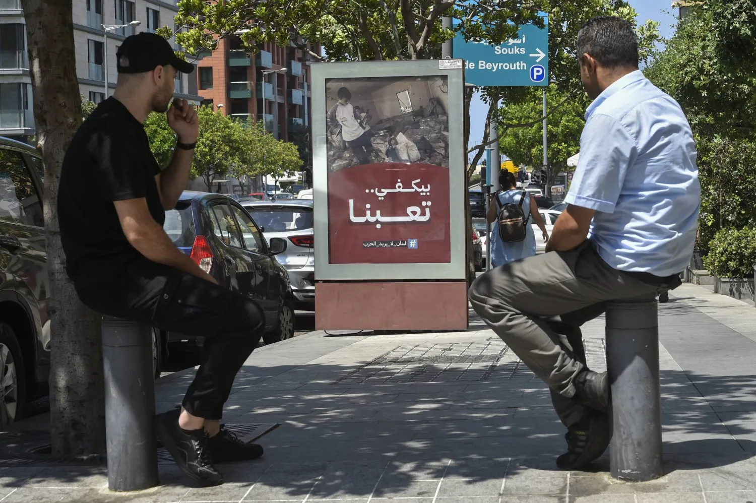 مواطنان لبنانيان ينظران إلى لوحة وضعت في وسط بيروت كتب عليها «بيكفي تعبنا.. لبنان لا يريد الحرب» (إ.ب.أ)