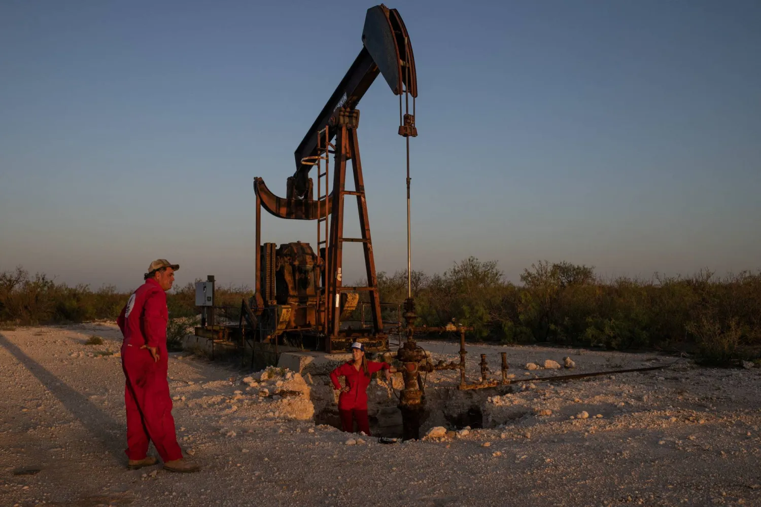 Hawk Dunlap, an oil well control specialist, and Sarah Stogner, an oil and gas lawyer, survey an excavated pumpjack with a leaking surface casing in Ward County, Texas, US, August 6, 2024. REUTERS/Adrees Latif 