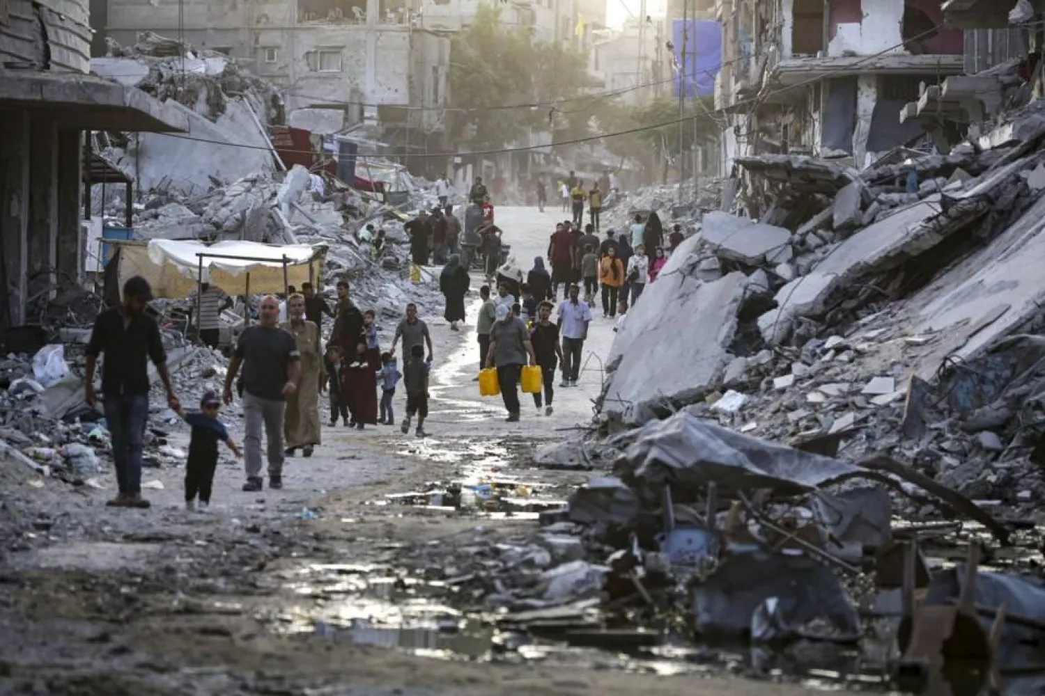 FILE - Palestinians displaced by the Israeli air and ground offensive on the Gaza Strip, walk through a dark streak of sewage flowing into the streets of the southern town of Khan Younis, Gaza Strip, on July 4, 2024. Health authorities and aid agencies are racing to avert an outbreak of polio in the Gaza Strip after the virus was detected in the territory's wastewater and three cases with a suspected polio symptom have been reported. (AP Photo/Jehad Alshrafi, File)

