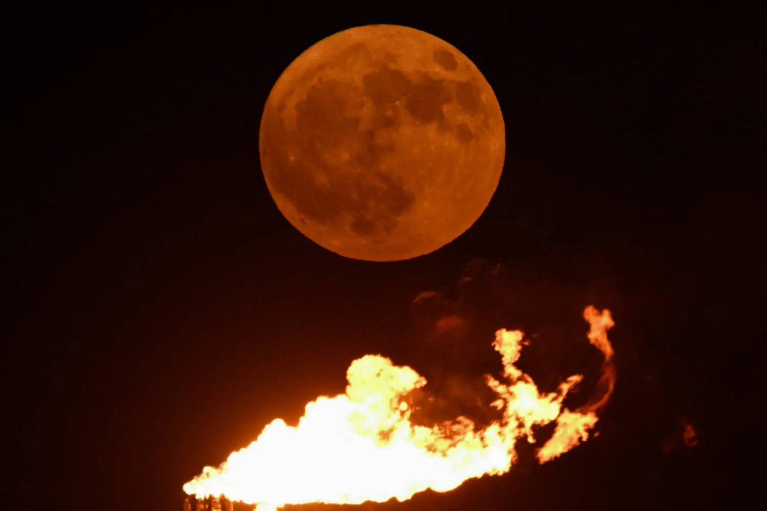 القمر الأزرق العملاق يظهر فوق حقل نفط بالقرب من مدينة البصرة العراقية (أ.ف.ب)