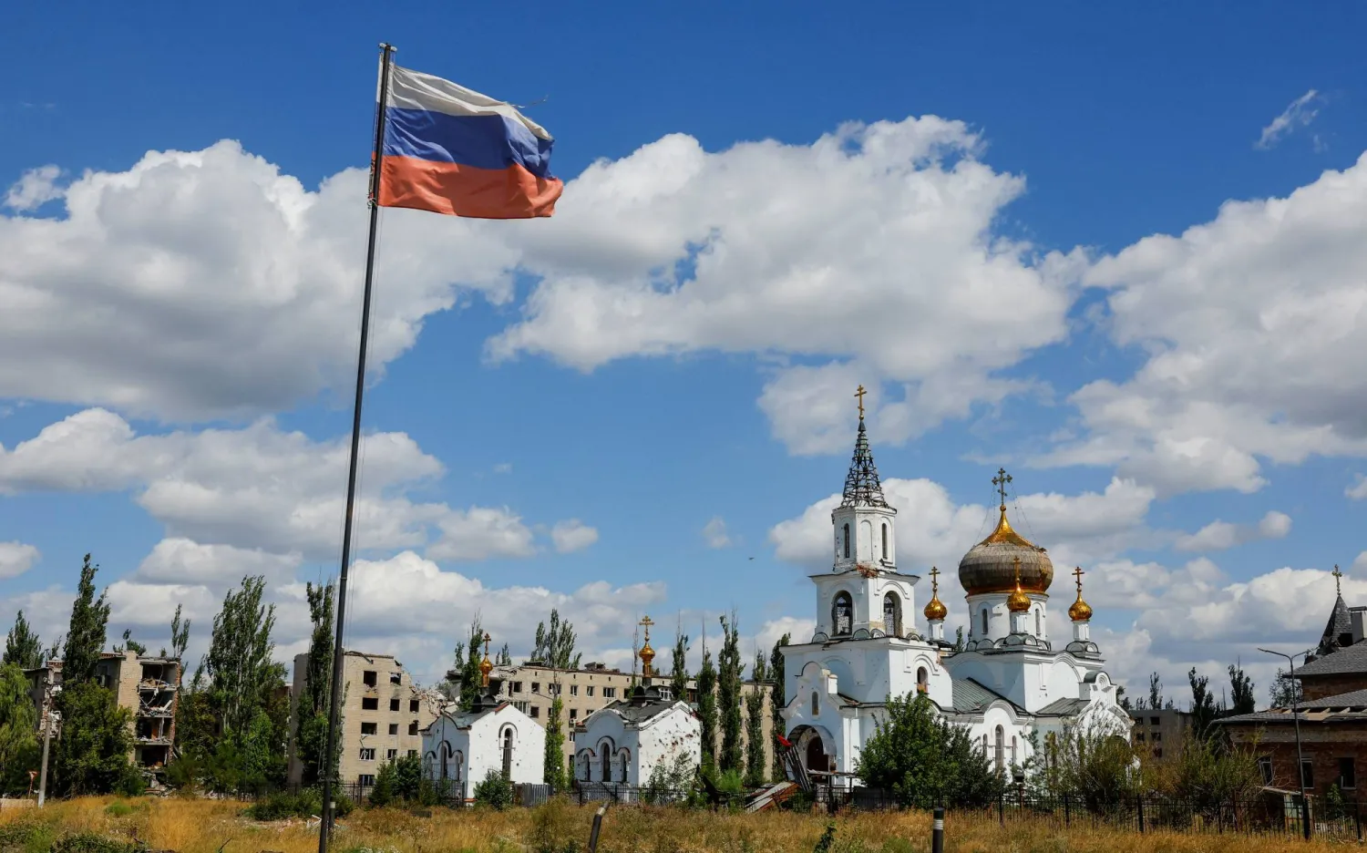 العلم الروسي يرفرف بالقرب من كنيسة تضرّرت بسبب الحرب في بلدة أفدييفكا بمنطقة دونيتسك الخاضعة للسيطرة الروسية (رويترز)
