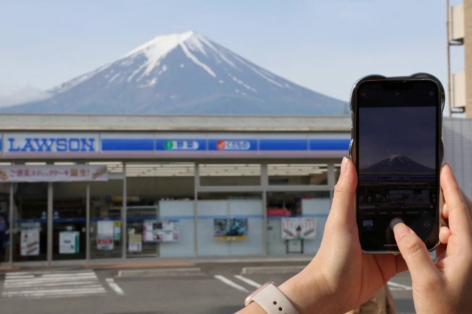 FILE PHOTO: A tourist takes a picture of Mount Fuji appearing over a convenience store in Fujikawaguchiko town, Yamanashi prefecture, Japan, May 21, 2024. REUTERS/Kim Kyung-Hoon/File Photo