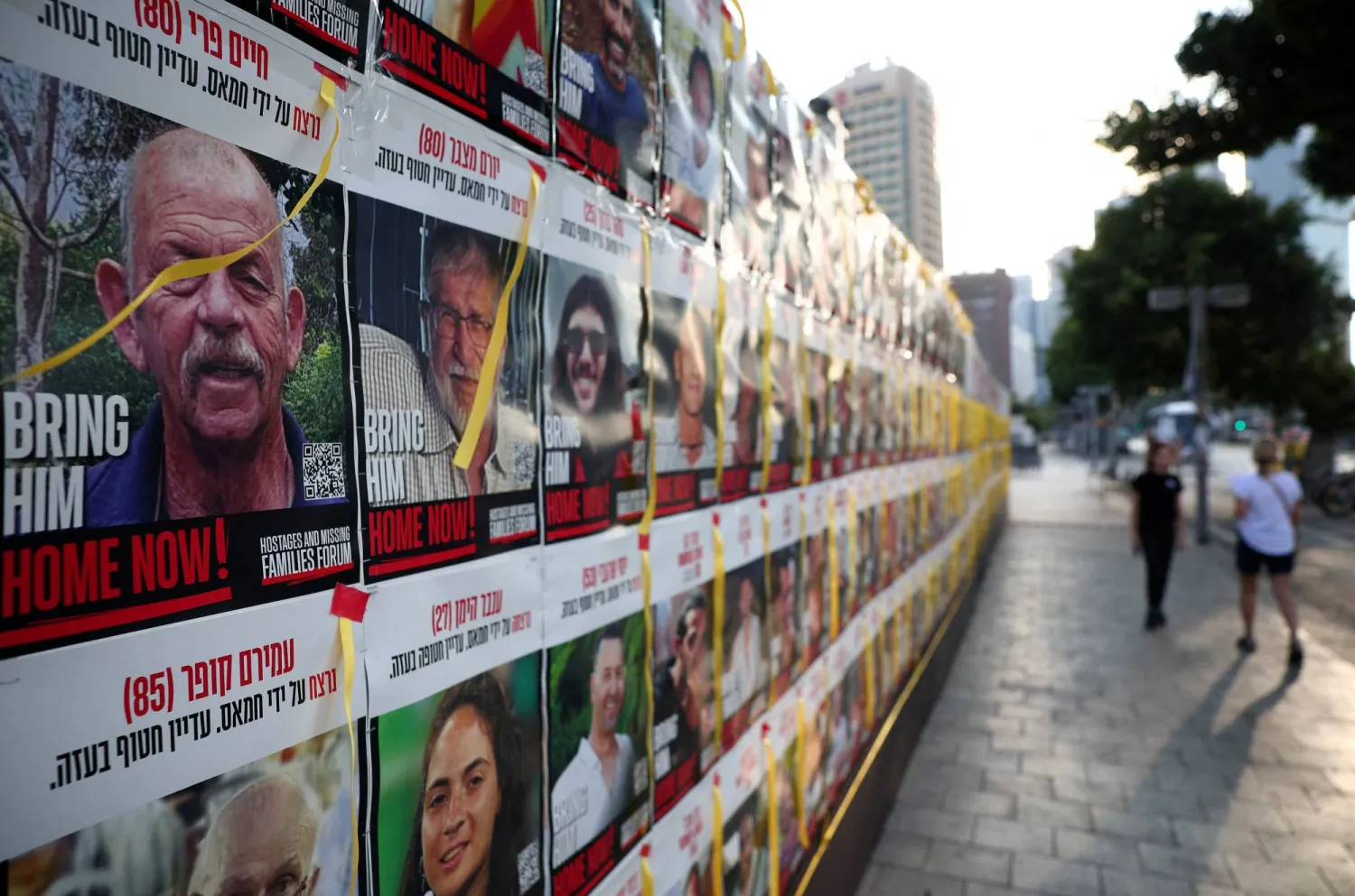أشخاص يسيرون بجوار جدار في تل أبيب يُظهر صور الرهائن الذين اختطفتهم حركة «حماس» (رويترز)