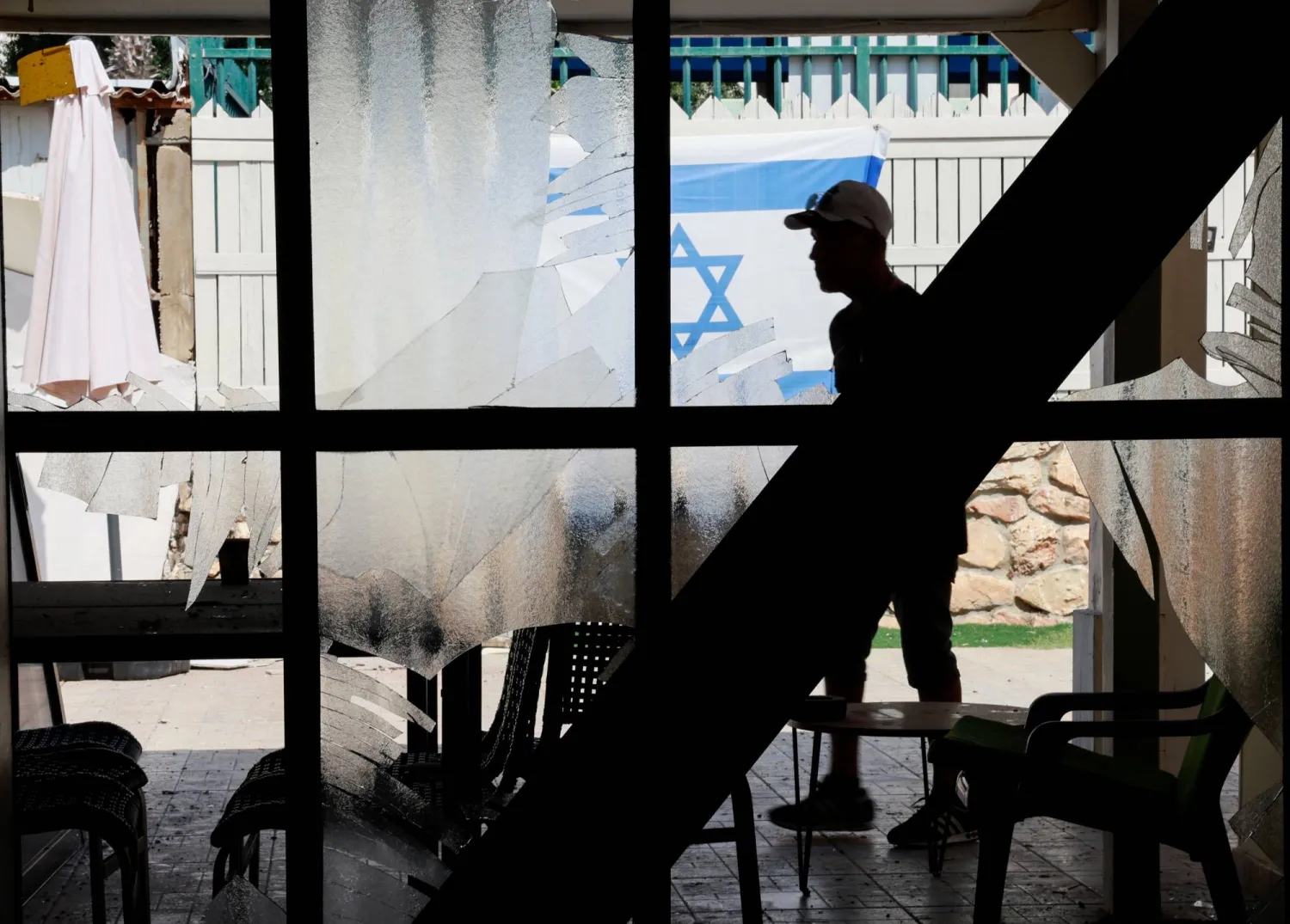 شخص يسير بالقرب من نوافذ محطمة في مبنى سكني متضرر بعكا شمال إسرائيل بعد أن أطلق «حزب الله» مئات الصواريخ والطائرات دون طيار باتجاه إسرائيل (رويترز)