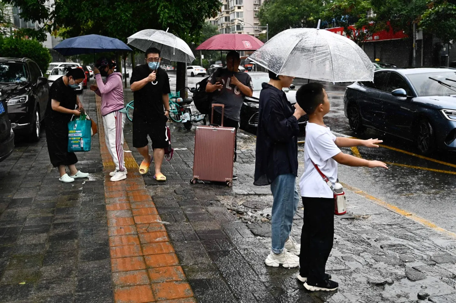 صينيون في العاصمة بكين يستخدمون المظلات تحت وابل من المطر الغزير (أ.ف.ب)