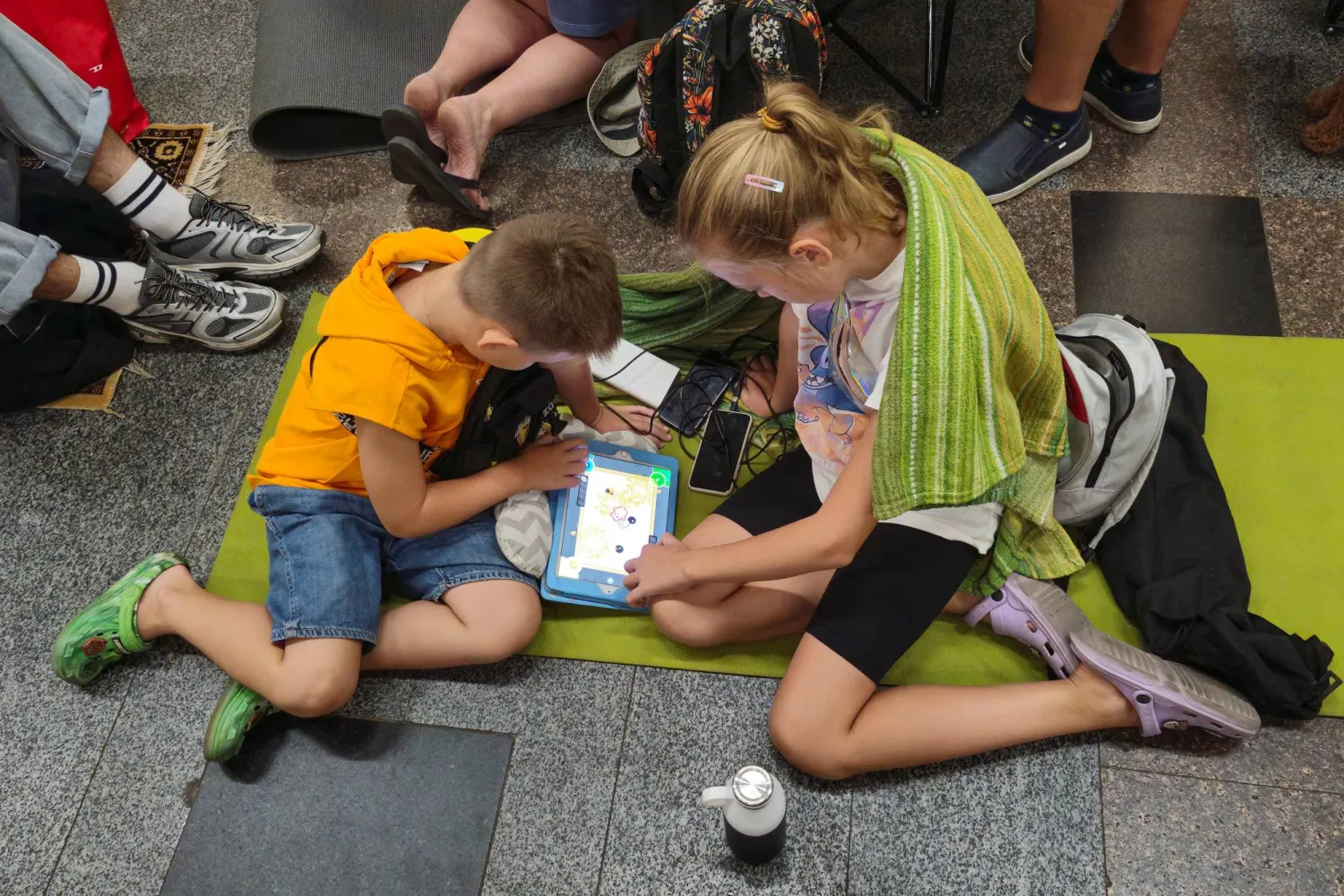 طفلان يستخدمان جهازاً لوحياً أثناء اختبائهما داخل محطة مترو وسط هجوم صاروخي روسي في كييف (رويترز)