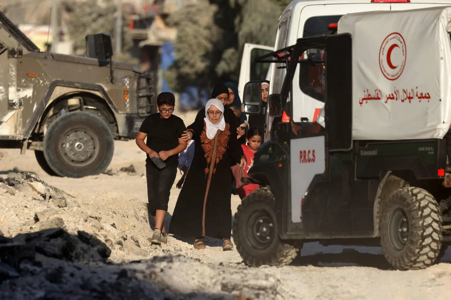 Members of a Palestinian family fleeing an Israeli raid in the Nur Shams camp near the city of Tulkarem in the Israeli-occupied West Bank, walk past Red Crescent ambulances stationed outside the camp on August 28, 2024. (Photo by JAAFAR ASHTIYEH / AFP)