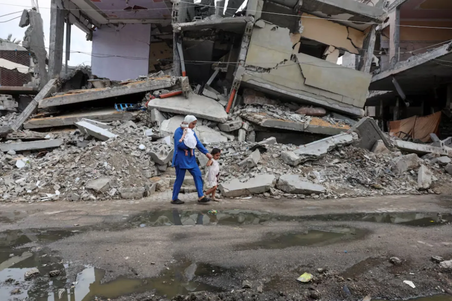 A displaced Palestinian mother, Wafaa Abdelhadi, walks past the rubble of a house destroyed in an Israeli strike as she returns to her shelter with her daughters Lynn and Roueida, after they got vaccinated against polio, in Deir Al-Balah, in the central Gaza Strip September 1, 2024/Reuters