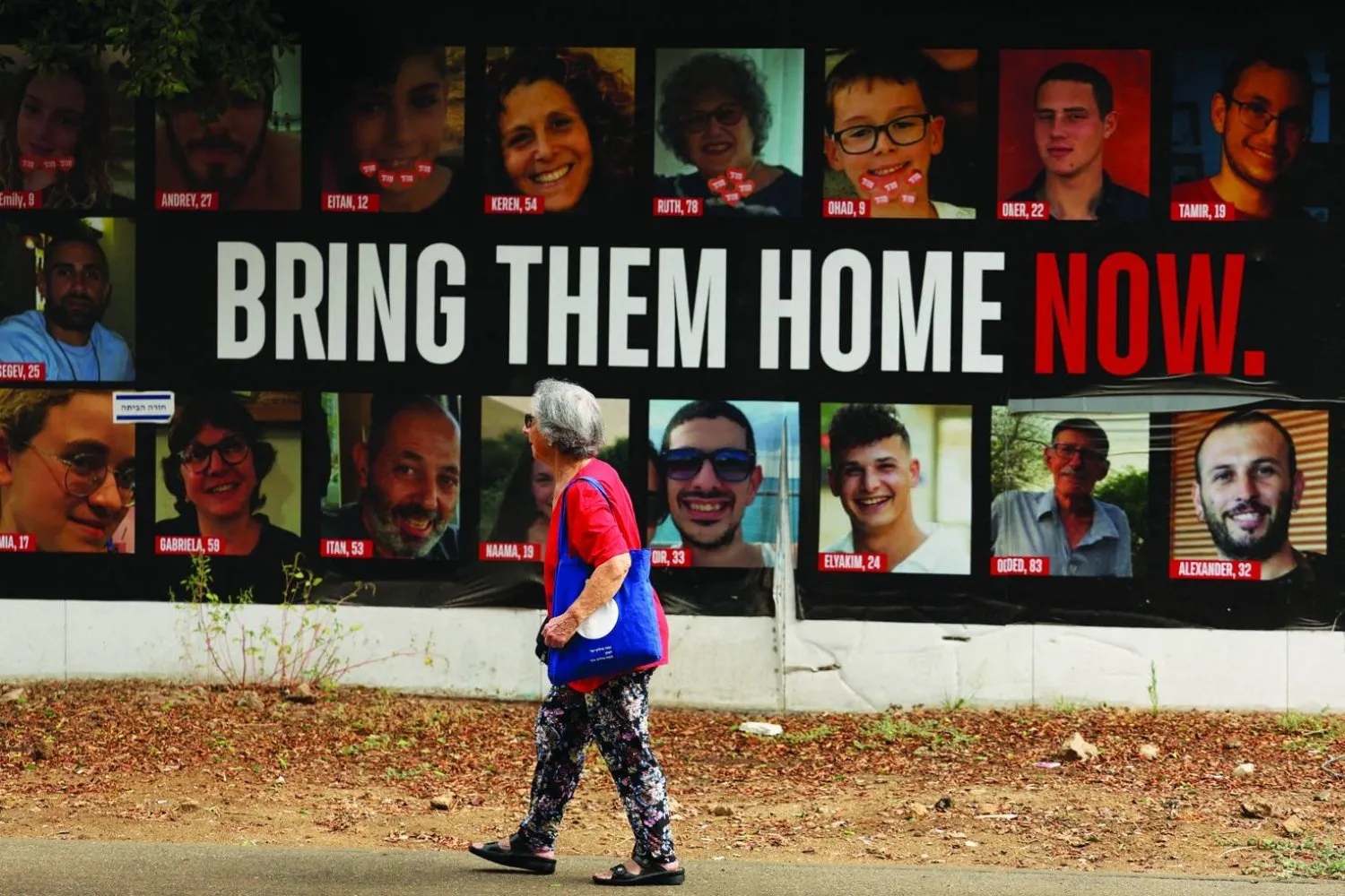 Hamas tarafından tutulan ve bazıları ölü bulunan İsrailli rehinelerin posterinin önünden geçen bir kadın (Reuters)