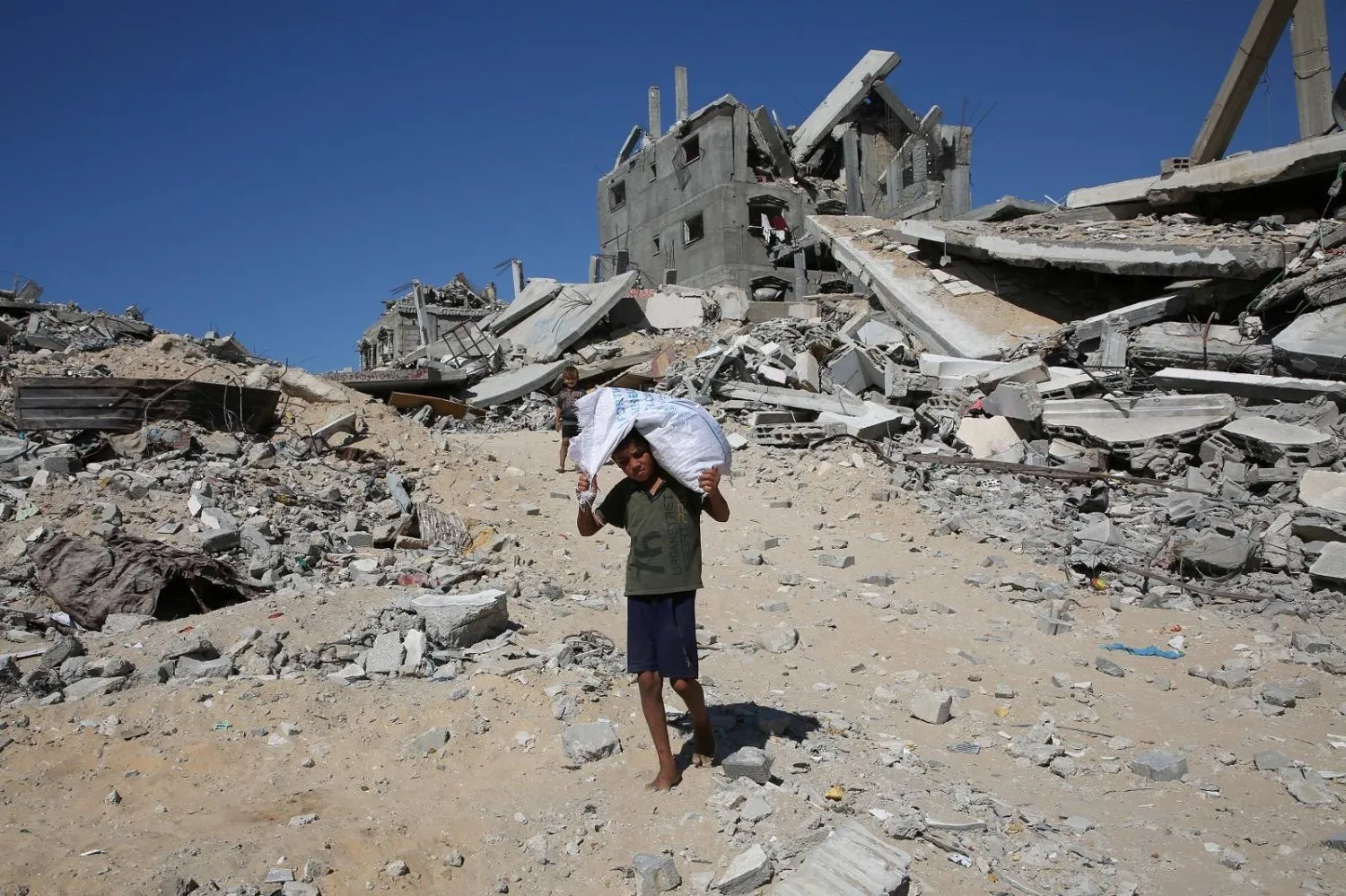 Gazze Şeridi'nin güneyindeki Han Yunus'ta İsrail saldırıları sonucu yıkılan evlerin enkazında çuval taşıyan Filistinli bir çocuk (Reuters)