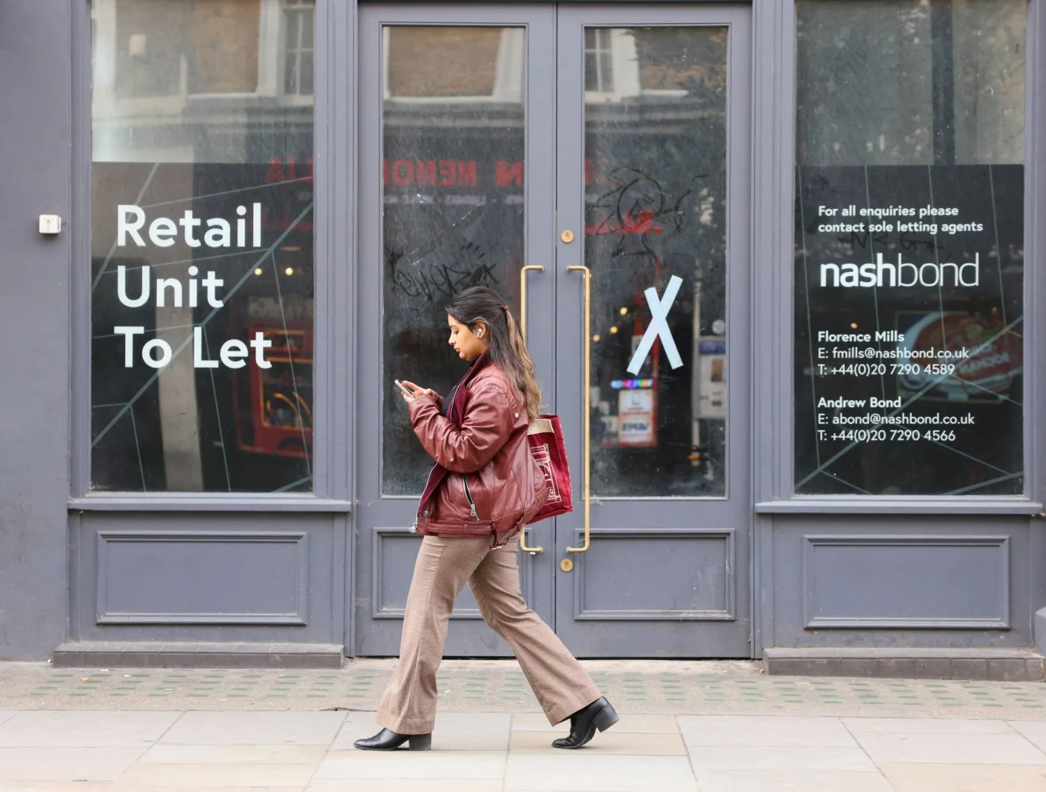 شخص يسير بجوار متجر مغلق في شارع كوينزواي هاي ستريت بلندن (رويترز)